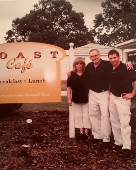 Historic photograph of three people beside the original Toast Café sign